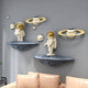 The White & Gold Orbit Odyssey Star Astronaut 3D Wall Art by Giant Sculptures features two astronauts with gold helmets on gray rocks, complemented by small ringed planets on a gray wall above a beige couch, offering captivating space-themed décor.