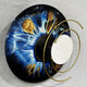 Aurelios Cosmic Blue Crystal Porcelain & Gold Orbit 3D Wall Art featuring a circular blue and brown iris design with a mirrored core and orbiting gold metal rings, shown against a plain grey background.