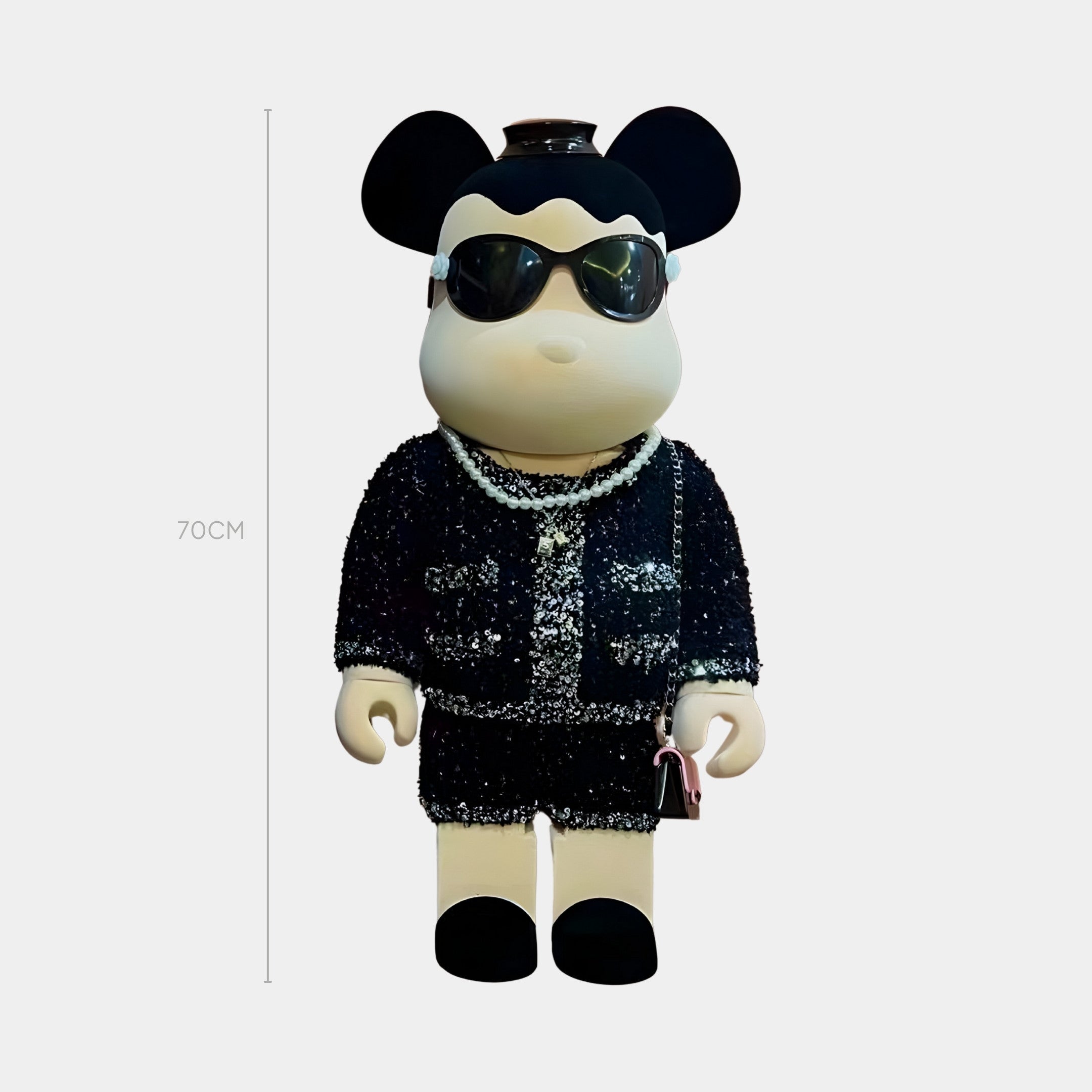 The Black Couture Bear Sculpture - 70cm by Giant Sculptures features round ears, a neutral expression, black sunglasses, a pearl necklace, bouclé jacket, black sequined skirt, and carries a small pink handbag.