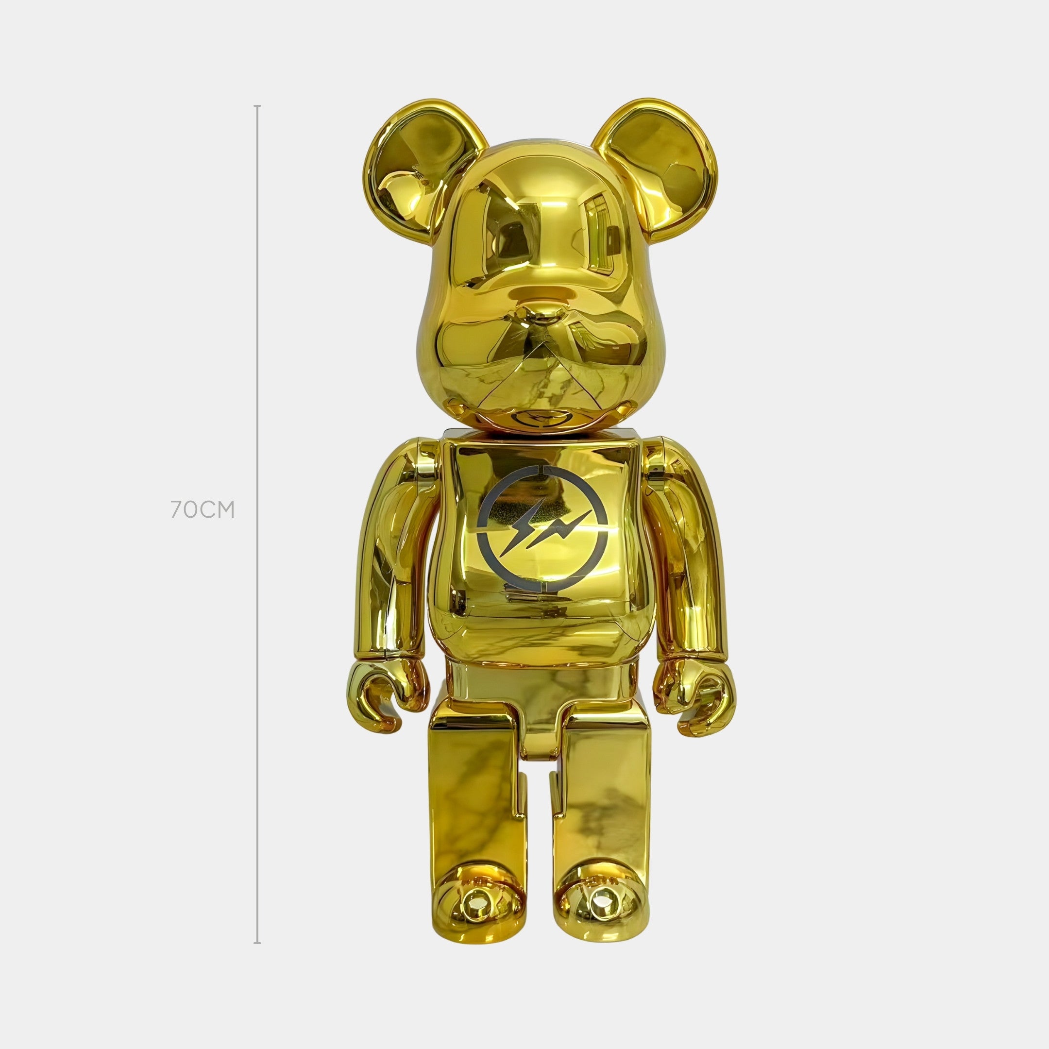 The Bolt Emblem Gold Bear Sculpture - 70cm by Giant Sculptures features a mirror gold finish, round ears, and a bold Bolt Emblem on its chest, standing out with its striking design against a plain white background.