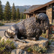 Life-Size Recumbent Bison Bronze Sculpture, 200cm, resting on a stone base outside a park visitor center with mountain and forest backdrop.