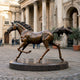 Large Traditional Galloping Horse Bronze Sculpture, 180cm, on a round plinth in a colonnaded courtyard with visitors nearby.