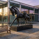 Large Traditional Standing Mare Bronze Sculpture, 260cm, mid-stride with a foal, mounted on a dark plinth in a courtyard beside a glass building and pool.