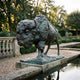 Monumental Charging Bison Bronze Sculpture by Giant Sculptures with green-blue verdigris patina, shown in profile on a stone plinth beside a formal garden pool.