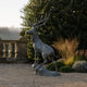 Life-Size Rearing Stag Bronze Sculpture by Giant Sculptures displayed on gravel beside a stone balustrade and garden border, antlers raised against foliage.