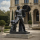 Life-Size Classical Nude Male Warrior Bronze Statue by Giant Sculptures in near-black patina, shield raised and sword lowered, displayed in a formal garden courtyard.