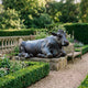 Life-Size Traditional Reclining Cow and Calf Bronze Sculpture by Giant Sculptures with verdigris patina, displayed on a stone plinth in a formal garden beside a wooden bench.