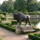 Life-Size Traditional Walking Bison Bronze Sculpture by Giant Sculptures on a stone plinth beside a garden bench, pond, and clipped hedges.