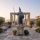 Monumental Classical Spartan Warrior Bronze Sculpture by Giant Sculptures, 250cm hoplite with crested helmet, spear, and shield on a stone plinth among ruins.