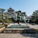 Monumental Armoured Samurai Warrior and Horse Bronze Sculpture by Giant Sculptures in verdigris patina on a stone plinth, displayed before a Japanese castle.