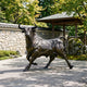 Monumental Charging Bull Bronze Sculpture by Giant Sculptures, 220cm, shown mid-charge on paved stone in a garden with a stone wall and timber pavilion.