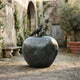 Monumental Crow on Apple Bronze Sculpture by Giant Sculptures with verdigris patina apple and black crow perched on the stem, displayed in a stone courtyard.