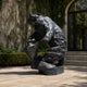 Monumental Rearing Grizzly Bear Bronze Sculpture by Giant Sculptures, shown seated on a rock with polished dark patina, displayed on a paved courtyard.