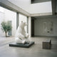 Giant Sculptures Contemporary Seated Polar Bear Bronze Sculpture 240cm in high-gloss white on a dark granite plinth in a minimalist gallery beside a courtyard.