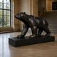 Life-Size Contemporary Walking Bear Bronze Sculpture by Giant Sculptures, dark patinated bronze on a low black plinth, displayed in a stone hall beside an arched window.