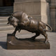 Large Traditional Charging Bull Bronze Sculpture by Giant Sculptures shown in side profile mid-lunge on a rocky plinth outside a stone-columned building.