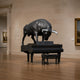 Monumental Contemporary Bull atop Grand Piano Bronze Sculpture by Giant Sculptures in matte black with silver-grey horns, displayed in a gallery beside framed paintings.