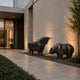 Monumental Bull and Bear Bronze Sculpture Set by Giant Sculptures in dark patina, displayed on gravel beside a modern stone entrance at dusk.