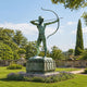 Monumental Classical Archer Warrior Bronze Statue, 350cm, green-patina bronze archer drawing a bow on a carved pedestal in a garden setting.