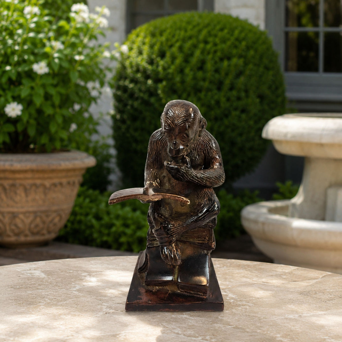 Traditional Reading Monkey Bronze Sculpture, 60cm, seated on stacked books holding an open volume, dark bronze finish, displayed outdoors on a stone table.