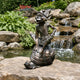 Traditional Laughing Goblin on Tortoise Bronze Sculpture, 80cm, shown outdoors on stone by a waterfall, warm brown cast bronze patina, goblin seated laughing with hand on hip.