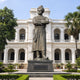 Monumental Traditional Standing Male Figure Bronze Statue, 400cm, folded arms and turban, on a stone base before a white colonnaded building.