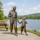 Life-Size Traditional Man and Boy Fishing Bronze Sculpture, 230cm, by Giant Sculptures, showing a man and boy holding fishing rods beside a lakeside path with a bench and water view.