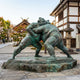 Life-Size Traditional Sumo Wrestlers Bronze Sculpture, 200cm, green-patina figures grappling on a stone base outside a traditional Japanese building.