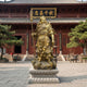Life-Size Traditional Guan Yu Warrior Bronze Statue, 220cm, gold-finished cast bronze figure with crescent blade on stone base outside a temple courtyard.