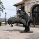 Monumental Three Charging Bulls Bronze Sculpture by Giant Sculptures in dark patina, mounted on a pedestal outside a stone building on a cobbled plaza.