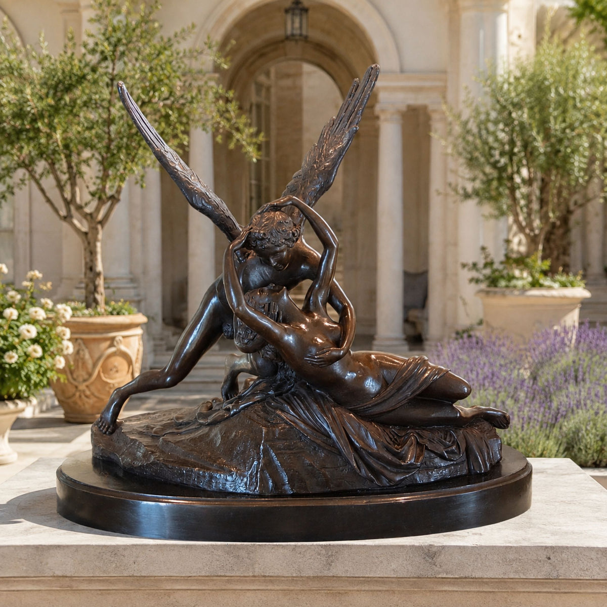 Large Classical Cupid and Psyche Bronze Sculpture, 120cm, on a round black base in a courtyard setting with columns and potted olive trees.