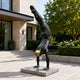 Large Contemporary Handstanding Male Figure Bronze Sculpture, 240cm, black patina finish with gold sphere, on a stone base in a modern courtyard setting.