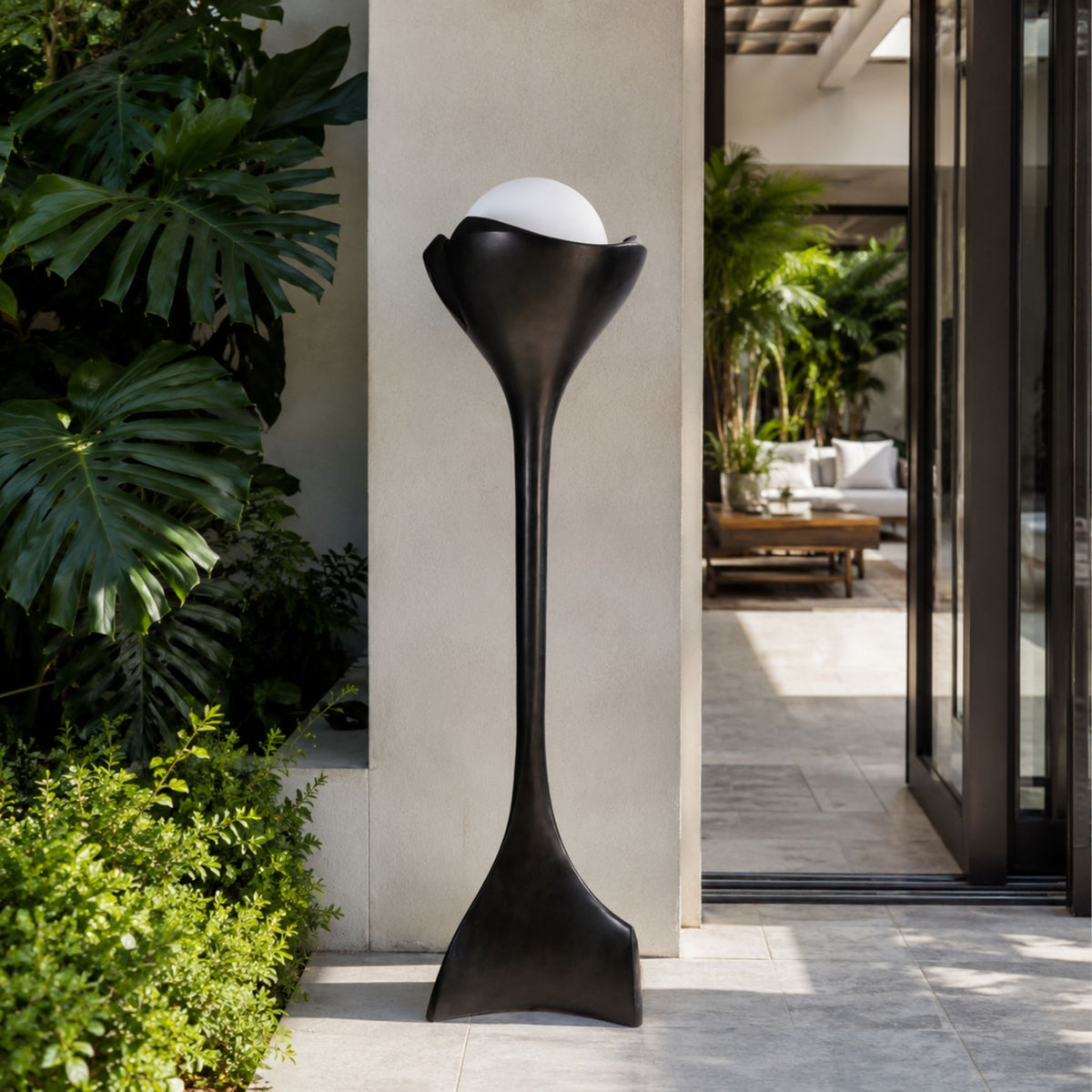 Black Pedestal Cup Sculpture - 175cm by Giant Sculptures, a cast bronze floor piece with a cup-shaped top holding a white sphere, shown against a courtyard wall near greenery.