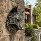 Traditional Wolf Head Bronze Sculpture, 70cm, mounted on a stone wall with golden-brown patina, set against an outdoor stone house exterior.