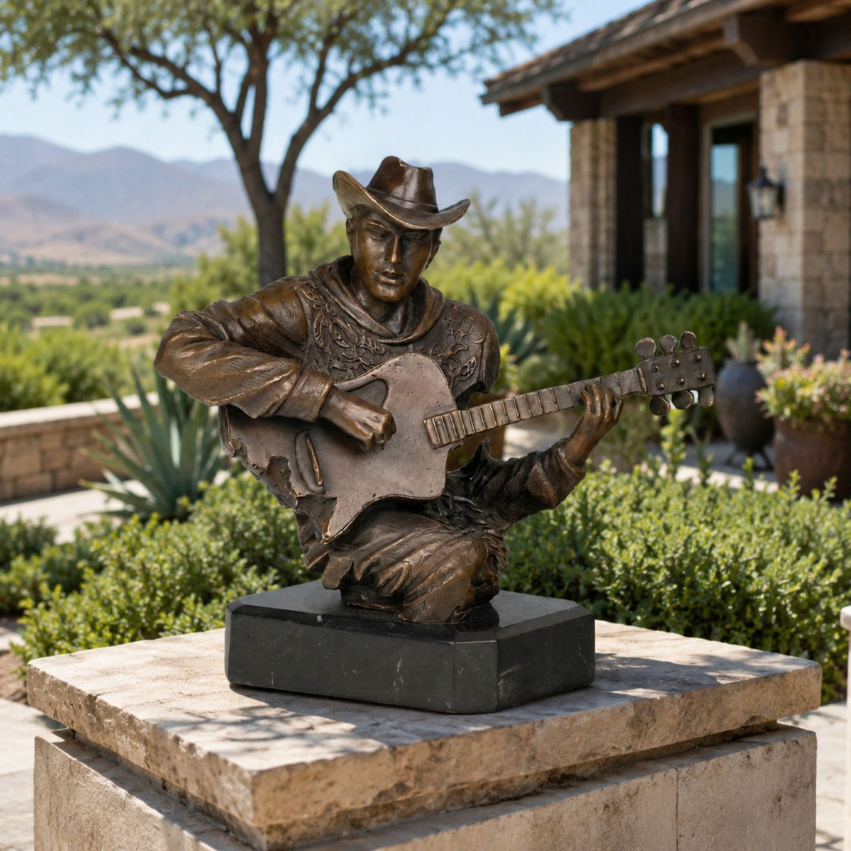 Traditional Cowboy Guitarist Bronze Bust, 70cm, on a black marble base, shown outdoors on a stone pedestal with a garden and hills backdrop.