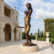 Monumental Classical Perseus and Medusa Bronze Sculpture, 300cm, on a round stone base outdoors, holding Medusa's head aloft beside a classical building and gardens.