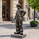 Life-Size Traditional Standing Tramp Figure Bronze Statue, 190cm, on a stone base along a city sidewalk with storefronts and a tree in the background.