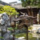 Traditional Chinese Dragon Head Bronze Sculpture (Arcing Tusks) - 45cm, side view with open jaws and flame-mane detail, displayed outdoors near a garden pond and stone rockery.