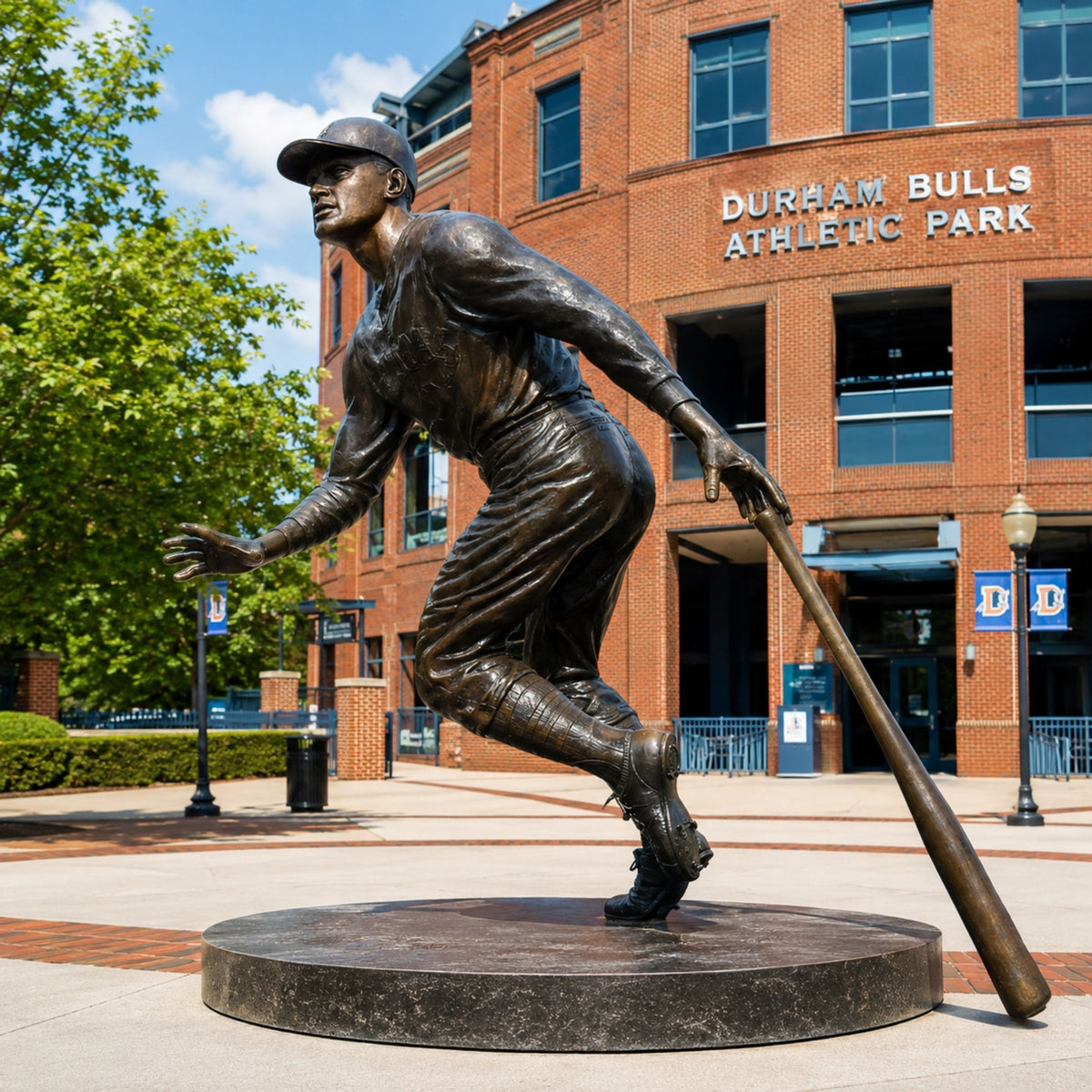 Life-Size Contemporary Baseball Player Bronze Statue, 250cm, on a round base outside Durham Bulls Athletic Park, captured mid-stride with bat in hand.