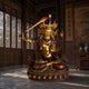 Monumental Traditional Manjushri Seated Bronze Sculpture, 300cm, gilded bronze figure in lotus pose with raised flaming sword, displayed on a lotus base in a wood-paneled hall.