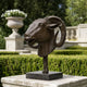 Traditional Ram Head Bronze Sculpture, 50cm, on a slender pole and dark marble base, displayed outdoors amid manicured hedges and stone garden décor.