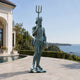 Large Classical Standing Poseidon Bronze Sculpture, 220cm, holding a trident on a poolside patio with sea and coastline in the background.