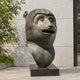 Monumental Contemporary Monkey Head Bronze Sculpture, 180cm, oversized bronze primate head with open mouth on a dark base, outdoors against a stone wall.