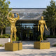 Life-Size Classical Muscular Nude Pair Bronze Sculpture, 260cm gold-toned figures in bodybuilding poses on plinths outside Iron Legacy Fitness entrance.