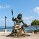 Monumental Classical Poseidon Bronze Sculpture, 450cm, muscular figure holding a trident and turtle atop a rocky, fish-adorned base by the seaside.
