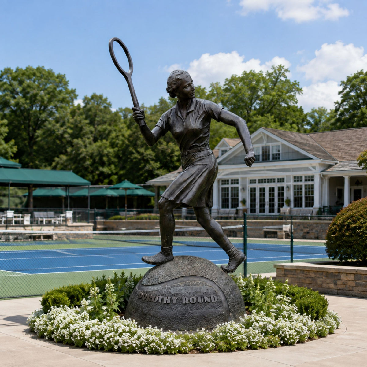 Monumental Female Tennis Player Bronze Sculpture, 220cm, mid-swing pose on a stone base, displayed outdoors near a tennis court and clubhouse.