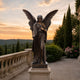 Life-Size Classical Standing Angel Bronze Sculpture, 220cm, wings spread wide, holding a palm frond, on a stone pedestal along a terrace balustrade at sunset.