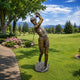 Life-Size Golfer Mid-Swing Bronze Sculpture, 220cm, on a stone base amid a golf course lawn with trees and mountains in the background.