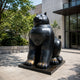 Monumental Contemporary Rotund Seated Cat Bronze Sculpture, 300cm, black bronze finish, seated on a base outside a glass-fronted building.