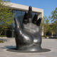 Monumental Contemporary Open Hand Bronze Sculpture, 450cm, black cast bronze palm with splayed fingers, installed outdoors on a paved plaza near a glass building.